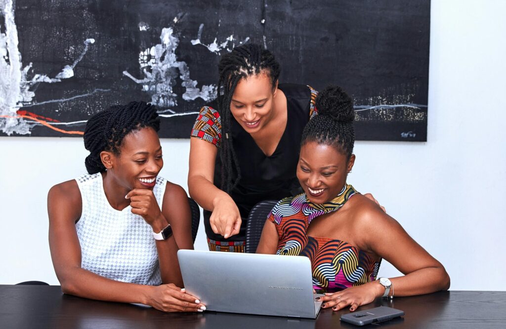 Image of three women smile and look at a laptop together, one standing and pointing at the screen, showing Huntsville Alabama safety for Black families.
