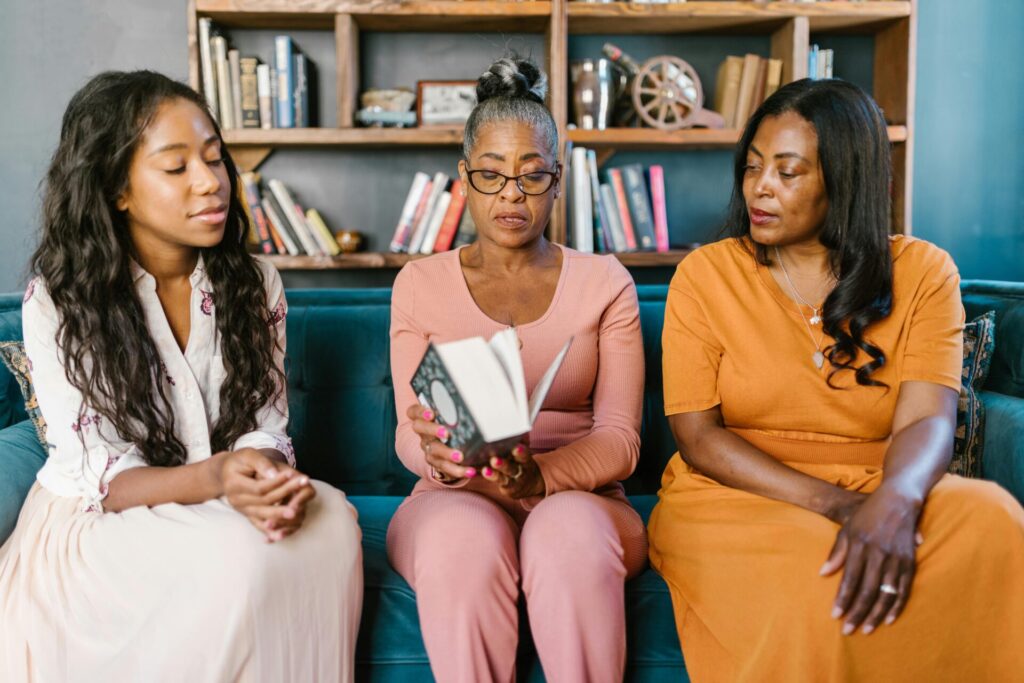 Image of three women sit on a couch, one reading a book aloud while the others listen attentively, representing black people safety in Huntsville.
