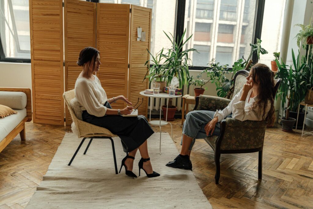 Image of two women having a therapy session in a cozy room with plants and natural light, showing mental load in a relationship.