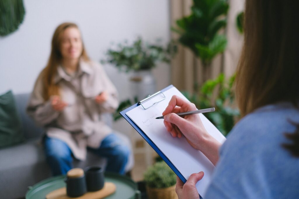 Image of a therapist taking notes on clipboard while listening to a woman during a counseling session.